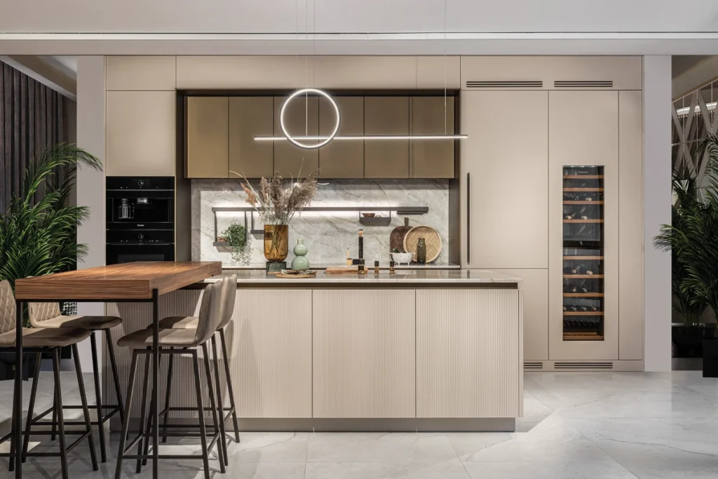 Nowoczesna kuchnia z wyspą w beżu, marmurowy backsplash, okrągła lampa LED, winiarka w słupku i wysokie hokery