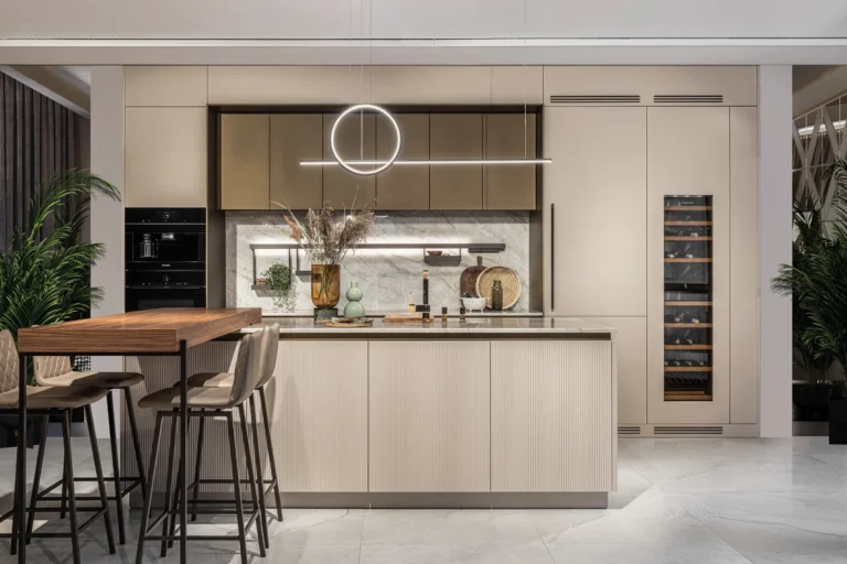 Nowoczesna kuchnia z wyspą w beżu, marmurowy backsplash, okrągła lampa LED, winiarka w słupku i wysokie hokery
