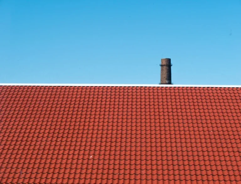 Czerwony dach z dachówki ceramicznej z kominem na tle błękitnego nieba