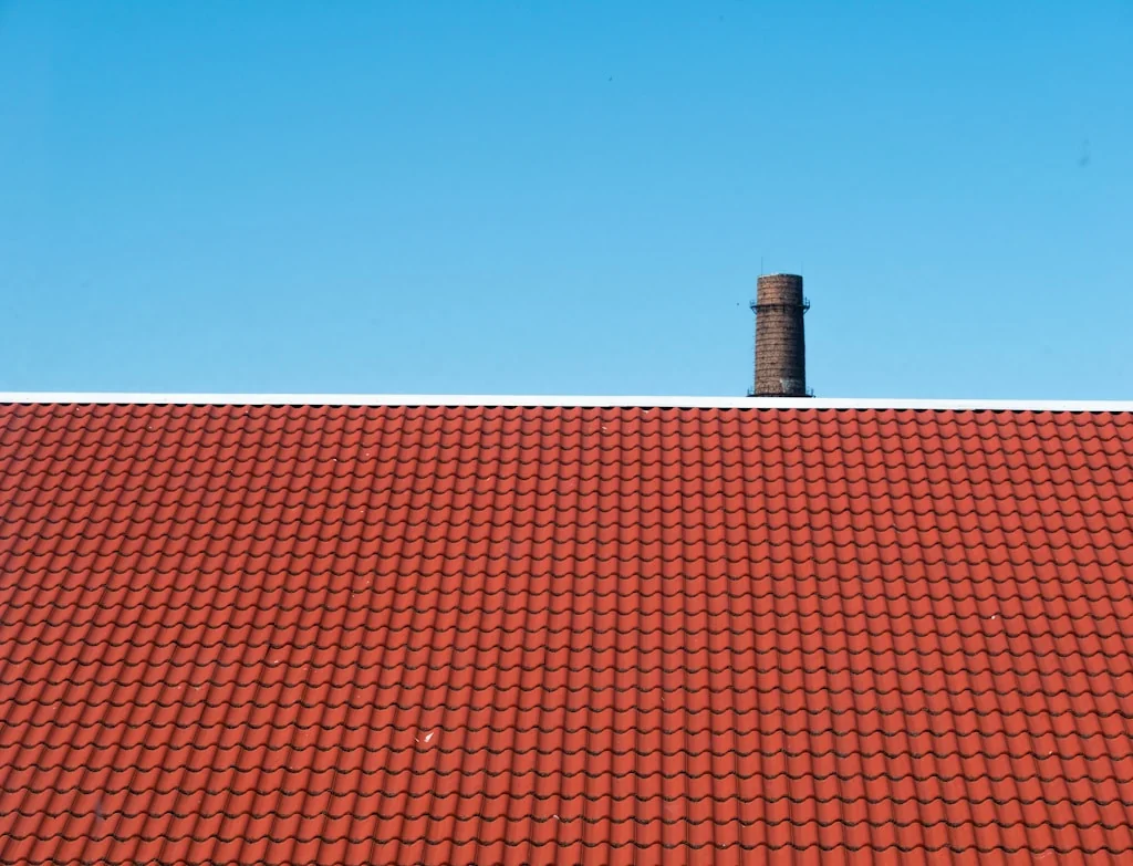 Czerwony dach z dachówki ceramicznej z kominem na tle błękitnego nieba
