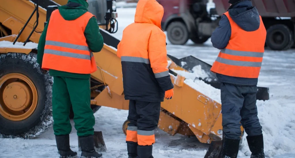 Brygada drogowa w odzieży zimowej i kamizelkach odblaskowych przy odśnieżarce.