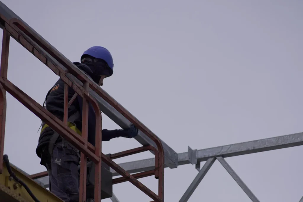 Pracownik na podnośniku montuje dźwigar hali namiotowej – prace na wysokości
