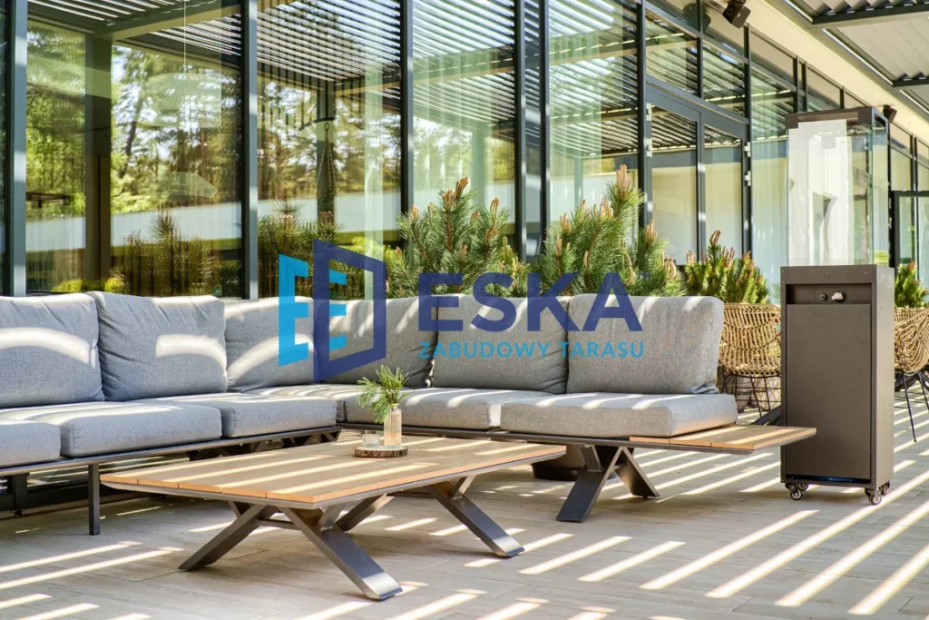 Nowoczesna pergola tarasowa ESKA z szarym kompletem wypoczynkowym przed przeszkloną elewacją