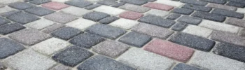 Zbliżenie na kostkę brukową w mozaikowym układzie – szare, białe i czerwone elementy nawierzchni.