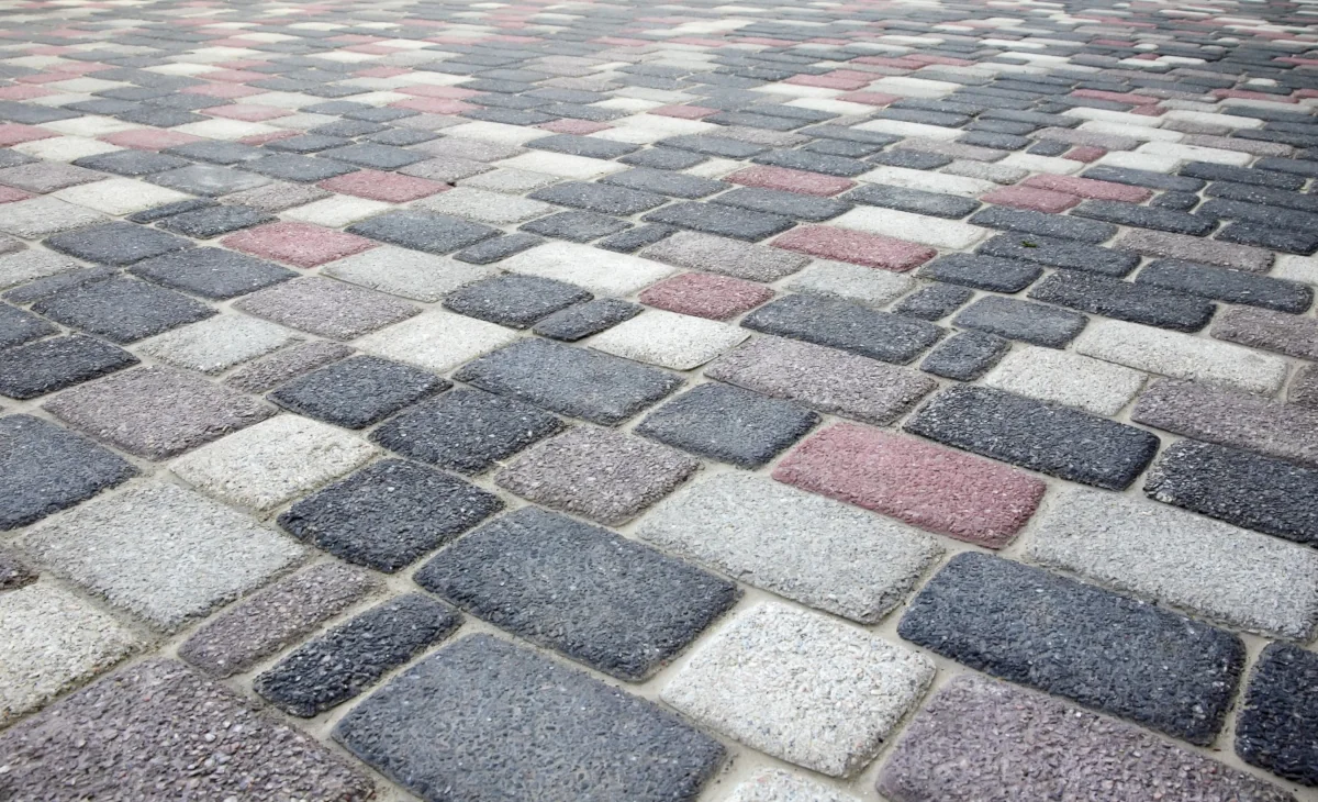 Zbliżenie na kostkę brukową w mozaikowym układzie – szare, białe i czerwone elementy nawierzchni.