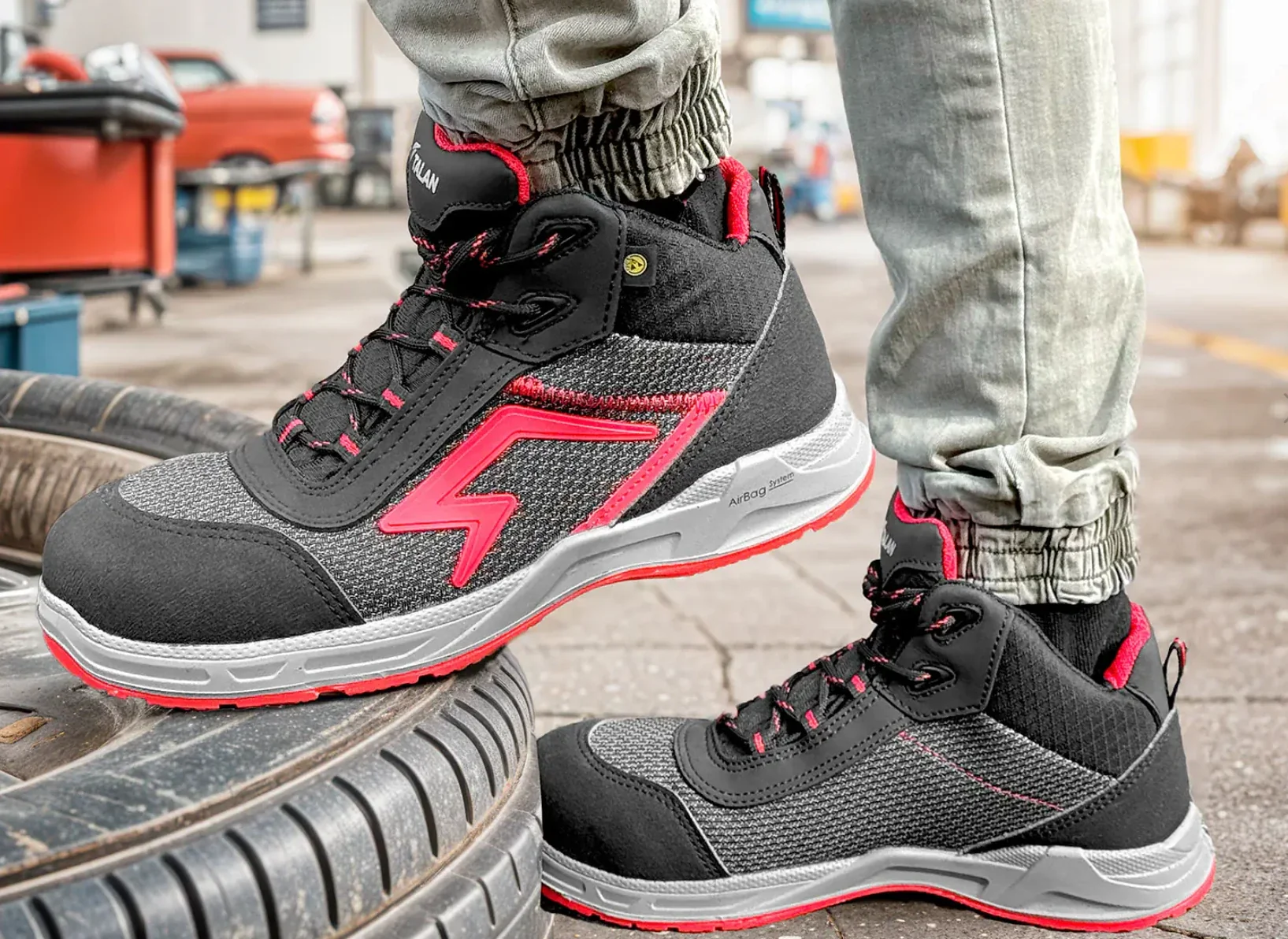 Czarno-czerwone buty robocze za kostkę z grubą podeszwą na industrialnym tle