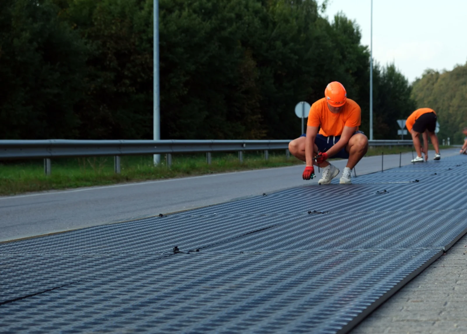 Pracownicy układają maty gumowe drogowe na jezdni przy drodze leśnej
